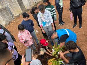 Plantios de árvores sendo feitos por crianças com ajuda de profissionais