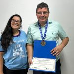 Aline Pinho, da UNG, e Wellington Alves, do GRU Diário, em entrega de comenda